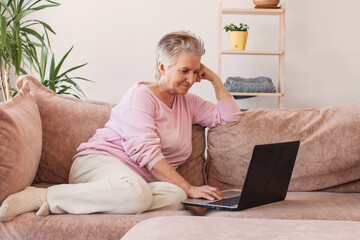 Older smiling 60s woman sitting at home on sofa