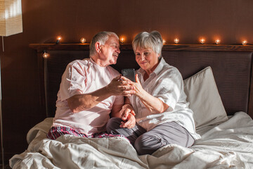 Happy mature couple lying on bed in bedroom and watching mobile phone