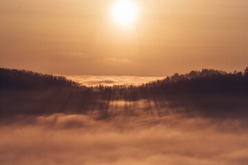 View of the sunset over a sea of clouds with a view of the sun passing through the forest on the other hill. Palkovicke hurky, moravskoslezský region, czech republic