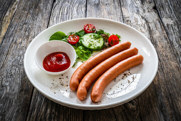 Breakfast - boiled sausages, bread and fresh vegetables served on wooden table
