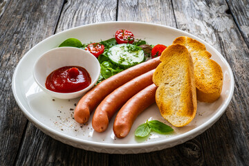 Breakfast - boiled sausages, bread and fresh vegetables served on wooden table
