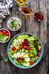 Tasty salad - leafy greens, camembert, pear,  pomegranate, cherry tomatoes and broad bean on wooden table
