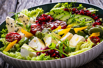 Tasty salad - leafy greens, camembert, pear,  pomegranate, cherry tomatoes and broad bean on wooden...