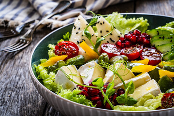 Tasty salad - leafy greens, camembert, pear,  pomegranate, cherry tomatoes and broad bean on wooden table
