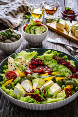 Tasty salad - leafy greens, camembert, pear,  pomegranate, cherry tomatoes and broad bean on wooden table
