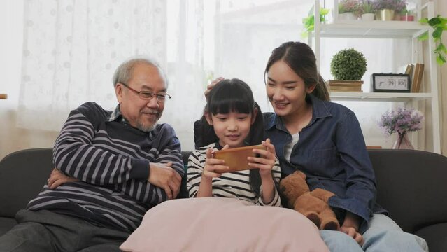 Asian happy family play time. little girl with grandparents together playing video games use joystick control enjoy laughing fun in living room home at night. Happy child happiness lifestyle concept.