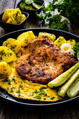 Fried pork chop with bone and egg, boiled potatoes,  cucumber on wooden table