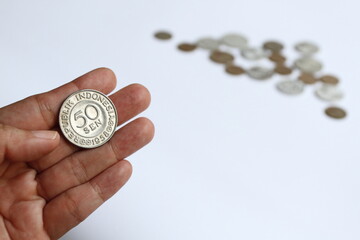 Someone fingers holding an Indonesian 1958 old coin of 50 cents Rupiah with blurry coins on the background.