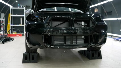 Fototapeta premium Car detailing. A black car without a bumper, prepared for pasting with a protective film. Disassembled car, ready for pasting with a protective film. A car without a bumper.