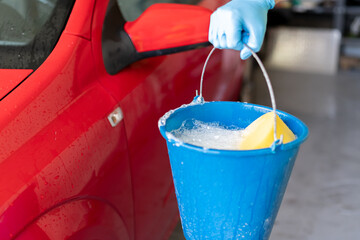 man's hand holding a bucket with soap to wash his car - obrazy, fototapety, plakaty