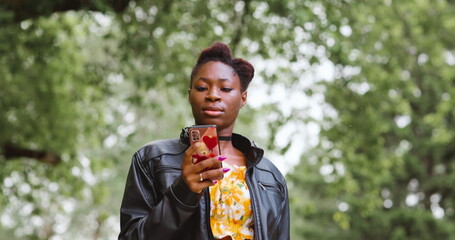 Naklejka premium African american woman with smartphone in hand internet communication walking on summer day in park.