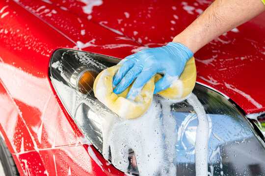 man's hand with blue glove washing the headlight of his car in the garage