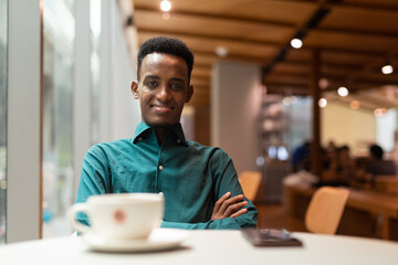 Fototapeta na wymiar Portrait of handsome young black man in coffee shop looking at camera