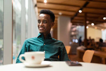 Fototapeta na wymiar Portrait of handsome young black man in coffee shop looking through window