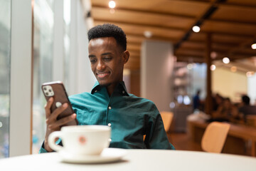 Portrait of handsome young black man in coffee shop using phone