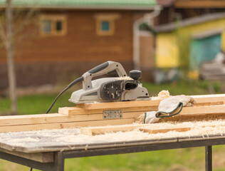 outdoors , an electric plane stands on planed boards next to protective gloves , a construction and repair concept
