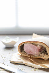 Schweinebraten im Brotteig auf Holztisch mit Fenchelsamen und Beilage grüne Sauce