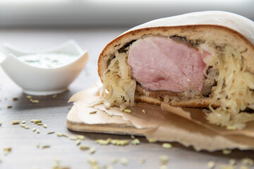 Schweinebraten im Brotteig auf Holztisch mit Fenchelsamen und Beilage grüne Sauce