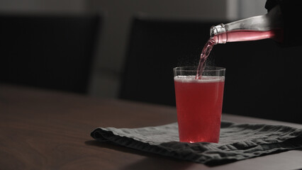pour pink drink in tumbler glass on wood table with copy space