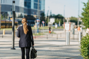 A female realtor in a blazer is walking with a laptop between skyscrapers.