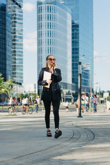 Female realtor in a blazer is strolling with a laptop in the financial district