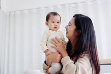 Mother holding a cute little boy with a happy smile. on the edge of the white curtain.