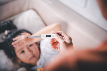 Sick kid. Mother parent checking temperature of her sick daughter with digital thermometer in...