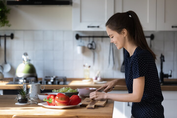 Happy positive chef blogger girl enjoying cooking, preparing salad for dinner, chopping fresh...
