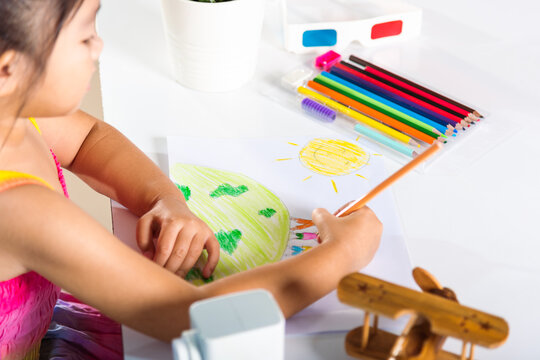 Asian cute kid preschooler sit on table smiling she draw picture with pencil at home, Happy child little girl colorful drawing family standing hold hands on planet earth on paper, earth day concept