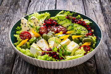 Tasty salad - leafy greens, camembert, pear, pomegranate, cherry tomatoes and broad bean on wooden...