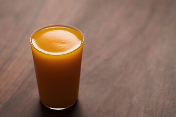 orange, pumpkin and carrot mixed juice in tumbler glass on walnut table