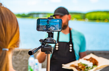 man chef gives an interview for a video blogger. videographer is filming the cook's story about...