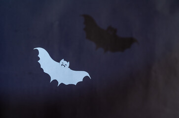 A white paper bat and its shadow on a gray wall. Halloween attribute cut out of a sheet of paper...