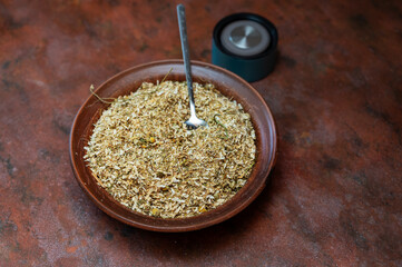 Dried Matricaria chamomilla flowers in bowl with spoon on kitchen table. A thermos lid in the background. The process of making an herbal tea or infusion of chamomile. Selective focus. Series part.