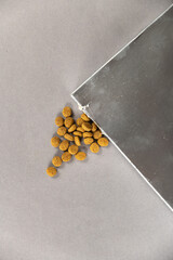 A silver rectangular box against a gray background. Pet food spilling out of the hole. Dry pelleted...