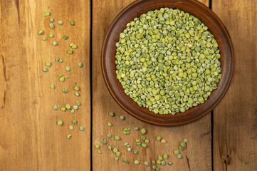 Dry split peas. Brown clay bowl. A scattering of green pea beans against a wooden background. Uncooked food. Healthy food. Close-up. Selective focus. Copy space for text and design elements.