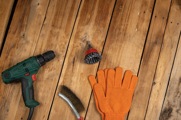 Electric drill, knot cup wire brush, metal brush and orange gloves. Hand and power tools lie on the boards. Woodworking. Top view. Selective focus.