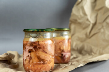 A glass jar of canned meat. Homemade chicken stew against a gray background. Slices of appetizing meat tightly packed in a transparent jar. Food ready to eat. Close-up. Selective focus.