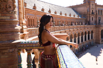 a beautiful adult belly dancer is leaning on a balcony in a square and is looking pensive and sad....