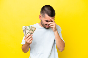 Young caucasian man taking a lot of money isolated on yellow background laughing