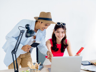 Happy Asian couple, young woman and man holding passport after using laptop computer together for flight booking with success feeling with smile for summer trip, ready to travel vacation concept.