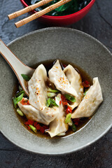 Close-up of a grey bowl with chili broth and steamed asian dumplings, vertical shot, selective focus