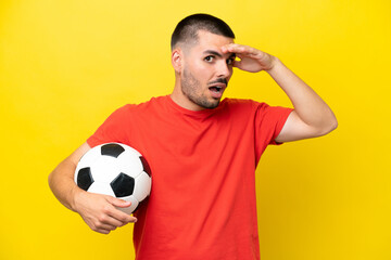 Young caucasian man playing soccer isolated on yellow background doing surprise gesture while looking to the side