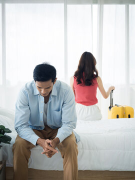 The anxiety of Asian couple lovers on the bed. Stressed man and young woman sitting on the bed with baggage wants to go away with relationship difficulties and feeling sad in the bedroom at home.