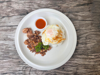 Fried pork with garlic and fried egg on rice in white plate, top view.