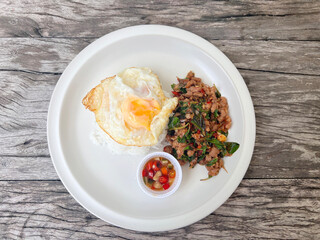 chicken basil with fried eggs in white plate, top view.
