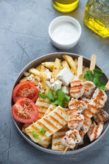 Plate with grilled haloumi, souvlaki skewers, potato fries with feta and greek yogurt, vertical shot on a grey concrete background