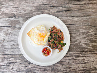 chicken basil with fried eggs in white plate, top view.