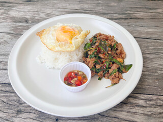 chicken basil with fried eggs in white plate, top view.