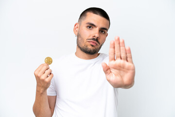 Young caucasian man holding a bitcoin isolated on white background making stop gesture